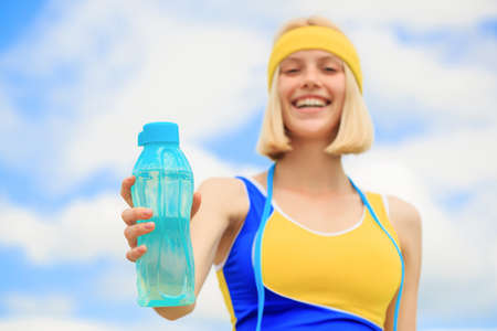 Healthy lifestyle concept. Woman in sportswear is holding a bottle of water. Young woman drinking water after run. Sports girl drinks water from a bottle on a sky background. Drinking during sportの写真素材