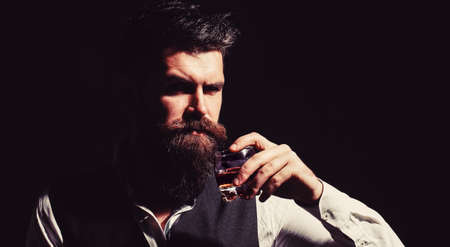 Man holding a glass of whisky. Sipping whiskey. Portrait of man with thick beard. Macho drinking. Degustation, tasting. Man with beard holds glass brandy. Bearded drink cognac. Sommelier tastes drinkの写真素材