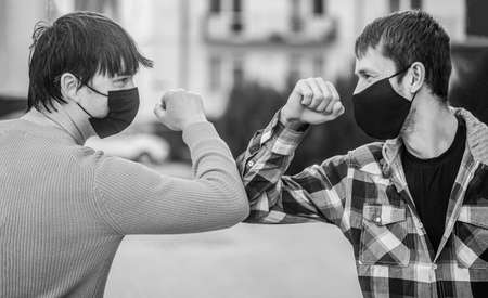 Friends in protective medical mask on his face greet their elbows in a quarantine. Elbow bump. Coronavirus, illness, infection, quarantine, medical mask, COVID-19. Elbows bump. Black and whiteの写真素材