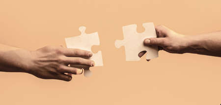 Two hands trying to connect couple puzzle with yellow background. Closeup hands of man connecting jigsaw puzzleの写真素材