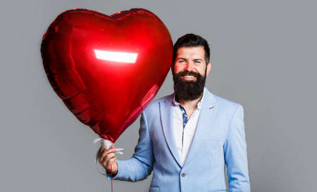 Happy man with heart shaped air balloons. Valentines Day. Red heart. Love hearts. Love and valentines day man holding heart smiling cute and adorable isolated. Valentine man with red air balloonの写真素材