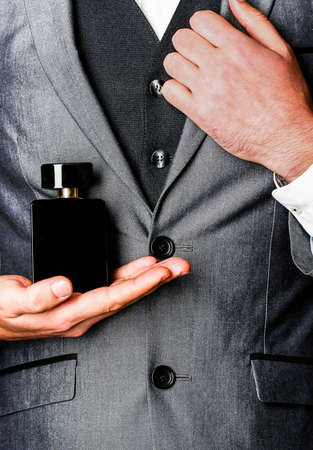 Man in formal suit, bottle of perfume, closeup. Fragrance smell. Men perfumes. Fashion cologne bottle. Man holding up bottle of perfume. Men perfume in the hand on suit backgroundの写真素材