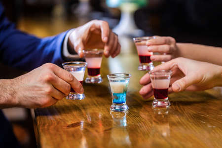Cocktail at the nightclub. Group friends tequila shot glasses in bar. Male hands glasses of shot or liqueur. Friends drink shot or liqueur. Five glasses of alcohol.Tequila shots, vodka, whisky, rumの写真素材