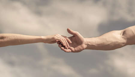 Giving a helping hand. Hands of man and woman on blue sky background. Lending a helping hand. Solidarity, compassion, and charity, rescueの写真素材