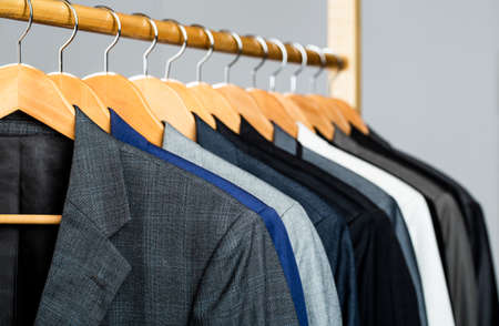 Suits for men hanging on the rack. Mens suits in different colors hanging on hanger in a retail clothes store, close-up. Mens shirts, suit hanging on rackの写真素材