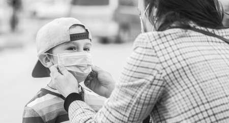 Mother puts her son a face protective mask outdoors. Stop coronavirus spreading. Coronavirus quarantine. Black and whiteの写真素材