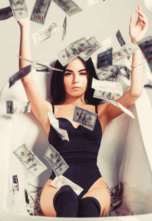 Millionaire woman lying in bedroom. Sexy woman lying in dollar bills. Rich sexy woman lies on money. Currency, women, winning. Sexy female and dollar billsの写真素材