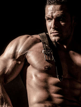 Muscular model sports young man on dark background. Fashion portrait of strong brutal guy. Leather...