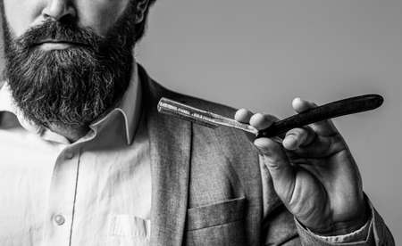Vintage straight razor. Man in barbershop. Handsome bearded hairdresser is holding a straight razor...