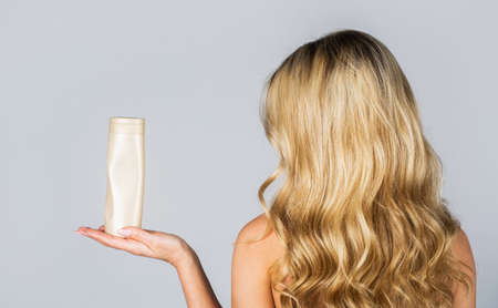 Woman hold bottle shampoo and conditioner. Woman holding shampoo bottle. Beautiful blonde girl with a bottle of shampoos in hands. Girl with shiny and long hair. Woman long hairの写真素材