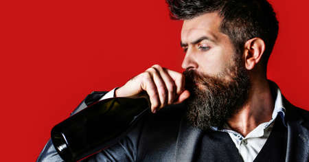 Man holding bottle with champagne, wine. Bearded man with a bottle champagne of and glass. The person holds a red wine bottle in a hand. Stylish male in tuxedo, suit, jacketの写真素材