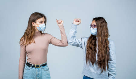 Elbow bump. Friends in protective medical mask on his face greet their elbows in a quarantine. Friends medical mask. People wear face mask. Friends bump elbows. Coronavirus epidemicの写真素材