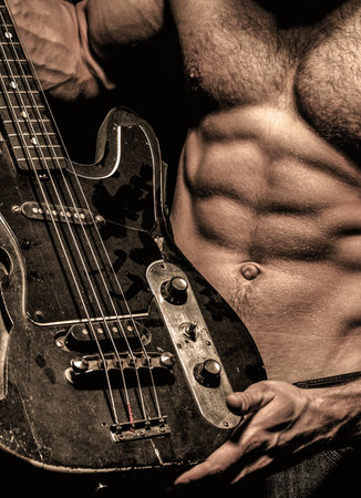 Electric guitar. Guitar. Instrument on stage and band. Strong, muscular, muscles man, bodybuilding. Music concept. Torso man. Play the guitar.の写真素材