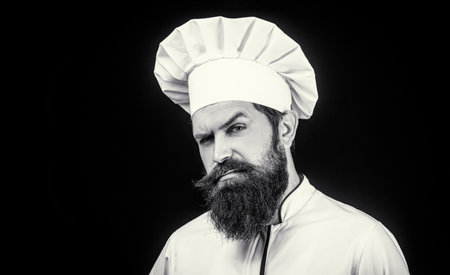 Cook hat. Confident bearded male chef in white uniform. Serious cook in white uniform, chef hat. Portrait of a serious chef cook. Black and whiteの写真素材