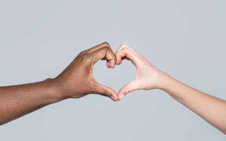 People different skin colors put their hands together making heart shape in white background. Charity, love and diversity - closeup of female and male hands of different skin color makingの写真素材