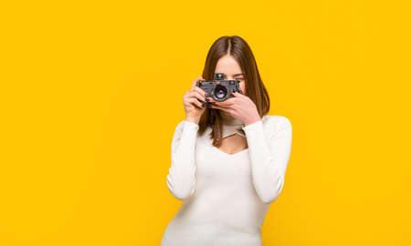 Woman holding camera over yellow background. Girl using a camera photo. Photographer camera photo, photographing girl joy make photography taking concept. Girl with a camerasの写真素材