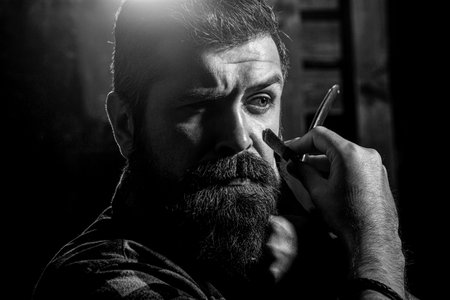 Vintage straight razor. Mens haircut. Man in barbershop. Handsome bearded hairdresser is holding a...