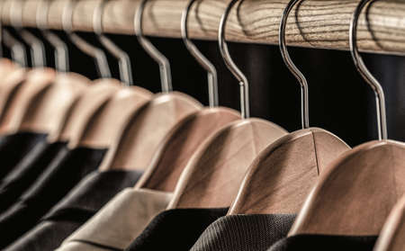 Mens suits in different colors hanging on hanger in a retail clothes store, close-up. Mens shirts, suit hanging on rack. Hangers with jackets on them in boutique. Suits for men hanging on the rackの写真素材