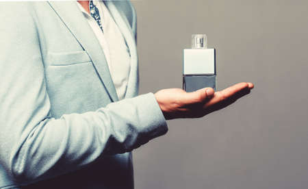 Masculine perfume, bearded man in a suit. Male holding up bottle of perfume. Perfume or cologne bottle and perfumery, cosmetics, scent cologne bottle, male holding cologne. Copy spaceの写真素材