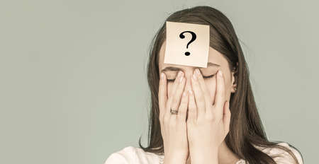 Confused female thinking with question mark on sticky note on forehead. rying woman with question...