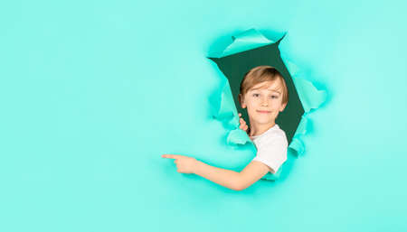 Kid looks through hole. Blonde boy looks through ripped paper. Boy in red paper hole pointing with...