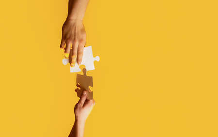 Two hands trying to connect couple puzzle with yellow background. Closeup hands of man connecting jigsaw puzzle. Business solutions, success and strategy conceptの写真素材