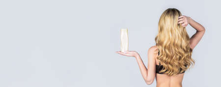Woman long hair. Woman hold bottle shampoo and conditioner. Woman holding shampoo bottle. Beautiful blonde girl with a bottle of shampoos in hands. Girl with shiny and long hairの写真素材