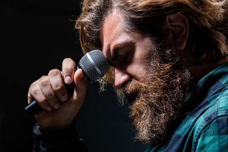 Male singing with a microphones. Man with a beard holding a microphone and singing. Bearded man in karaoke sings a song into a microphone. Male attends karaoke. Bearded man singing with microphoneの写真素材