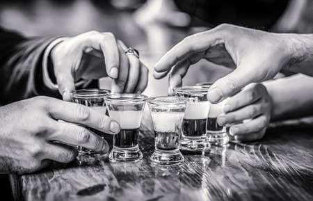Tequila shots, vodka, whisky, rum. Cocktail at the nightclub. Group friends tequila shot glasses in bar. Male hands glasses of shot or liqueur. Black and whiteの写真素材