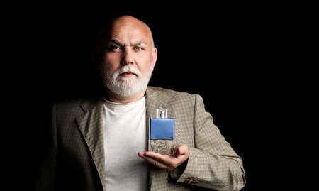 Masculine perfume, bearded old man in suit. Male holding up bottle of perfume. Aged man perfume,...