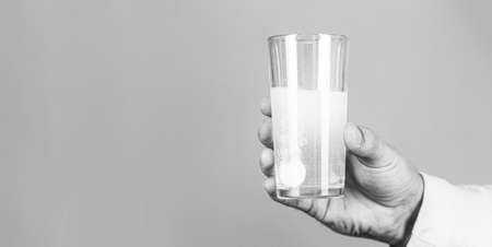 Glass of water tablet. Glass with efervescent tablet in water with bubbles. Close up of man holding a pill. Black and whiteの写真素材