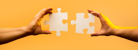 Business solutions, success and strategy concept. Two hands trying to connect couple puzzle piece on yellow background. Holding puzzle. Teamwork conceptの写真素材