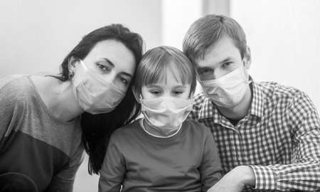 Young family in safety medical masks. Prevention coronavirus. Stay at home. Home quarantine. Coronavirus epidemic. Parents and kid wearing a surgical mask. Black and whiteの写真素材