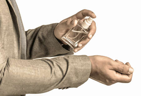 Fashion cologne bottle. Fragrance smell. Men perfumes. Handsome man in formal suit and with bottle of perfume, closeup. Man holding up bottle of perfume. Men perfume in the hand on suit backgroundの写真素材