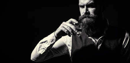 Attractive man with a whiskey. Handsome bearded man with stylish hair mustache and beard drinking brandy or whiskey from glassの写真素材