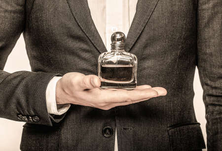 Man in a suit holding a bottle of perfume isolated on white background. Perfume or cologne bottle and perfumery, cosmetics, scent cologne bottle, male holding cologne. Male holding up bottle perfumeの写真素材