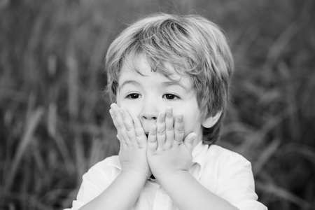 Funny child boy with hands close to face isolated on green background. Child expressing surprise with his hands in his face. Smiling amazed or surprised child boy. Shocked and surprised boyの写真素材