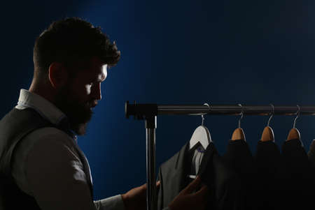 Man in suit. Shirts and suits in a male luxury store. Row of man suit jackets on hangers. Tailor in his workshop, designer. Bearded man in suit. Client is elegant guyの写真素材