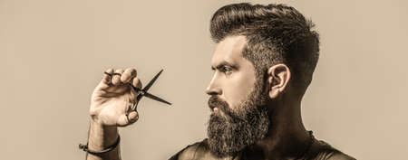 Male in barbershop, haircut, shaving. Bearded man isolated on gray background. Mans haircut in barber shop. Barber scissors, barber shop. Barber scissors. Vintage barbershop, shavingの写真素材