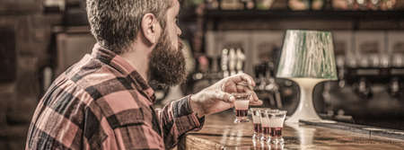Drinking alcohol into shot glasses in a nightclub or bar. Bearded man shots cocktail. Tequila shots, vodka,whisky, rum. Barman in pub. Tequila shot. Colorful cocktails at the barの写真素材