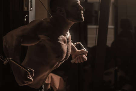 Muscular man workout in gym doing exercises for chest, cable crossover. Strong male torso abs. Fitness man execute exercise with exercise-machine Cable Crossover in gym. Man with big muscles in gymの写真素材
