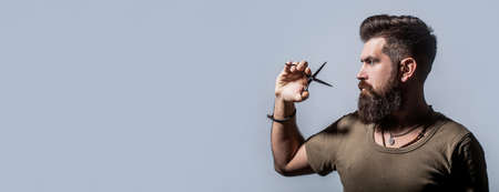 Male in barbershop, haircut, shaving. Bearded man isolated on gray background. Mans haircut in barber shop. Barber scissors, barber shop. Barber scissors. Vintage barbershop, shavingの写真素材