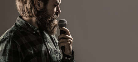 Bearded man in karaoke sings a song into a microphone. Male attends karaoke. Bearded man singing with microphone. Male singing with a microphonesの写真素材