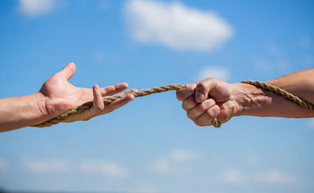 Rope, cord. Hand holding a rope, climbing rope, strength and determination. Rescue, help, helping gesture or hands. Conflict tug of warの写真素材