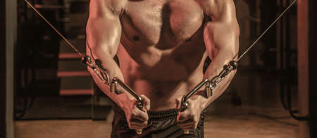 Abs and biceps. Fitness man execute exercise with exercise-machine Cable Crossover in gym. Handsome...