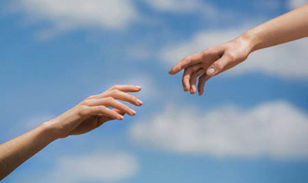 Two woman hands reaching towards each other on isolated sky background. Helping hand outstretched, salvation. Close up help hand. Two hands, helping arm friend, teamwork. Helping hand.の写真素材