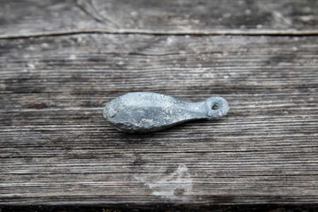 A piece of lead from fishing equipment lies on a weathered wooden surface