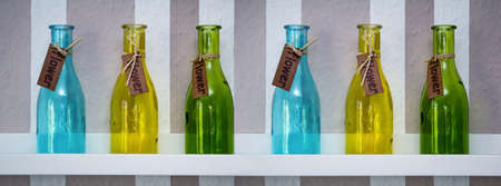 Six differently colored glass bottles are on a shelf.