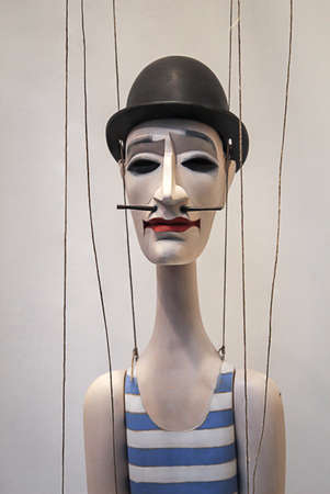 A wooden figure with a pointed beard and a bowler has hangs on threads.