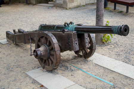 An old cast iron cannon with spoked wheels high above a town.の写真素材